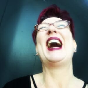 person with short purple hair, cat eye glasses, hard thrown back laughing uproariously